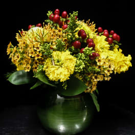 Yellow floral arrangement with red berry accents in a green glass vase