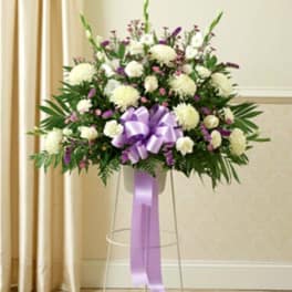 White and purple floral spray on a clear stand with a lavender ribbon