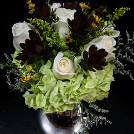 White roses and green hydrangeas in a silver vase with dark accent flowers