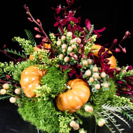 Orange pumpkins in a low floral arrangement with burgundy blooms and berries