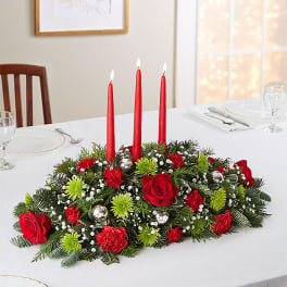 Red candle centerpiece with roses and greenery on a dining table