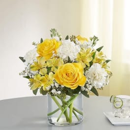 Yellow roses and white flowers arranged in a clear glass vase