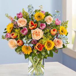Mixed bouquet of sunflowers, roses, and tulips in a clear glass vase