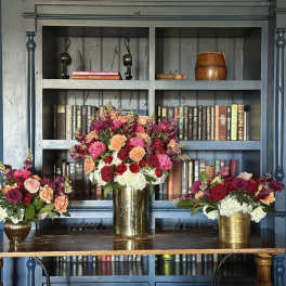 Three floral arrangements in gold vases on a table