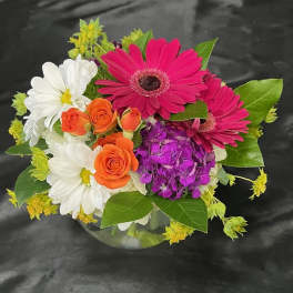 Bouquet of pink gerbera daisies, white daisies, and orange roses in a glass vase