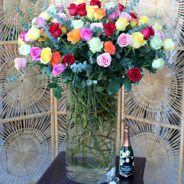 Mixed roses in a tall glass vase with a champagne bottle and candle