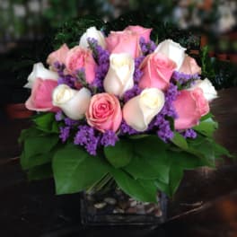 Pink and white roses arranged in a square glass vase with purple filler