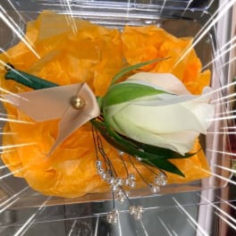 White rose boutonniere with ribbon and pearl accents on orange tissue