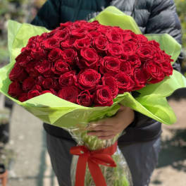 Large bouquet of red roses wrapped in bright green paper with a red ribbon