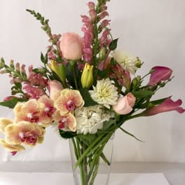 Mixed bouquet in a clear glass vase with pink roses, orchids, and white blooms