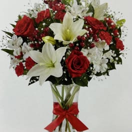 Red roses and white lilies in a clear glass vase with a red ribbon