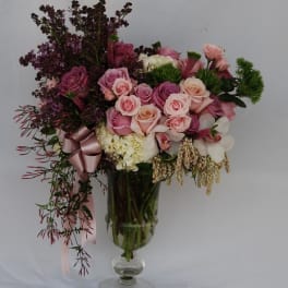 Pink and white rose bouquet in a clear glass vase with a ribbon
