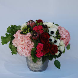 Mixed bouquet of roses, hydrangeas, and anemones in a silver vase
