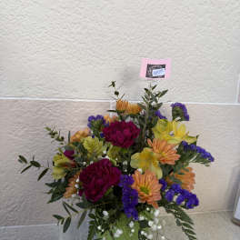 Mixed bouquet in a green container with orange, yellow, purple, and magenta flowers