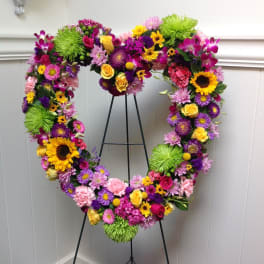 Heart-shaped floral wreath on a black stand with bright mixed flowers