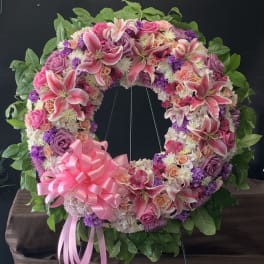 Heart-shaped floral wreath with pink lilies, roses, and a pink ribbon bow