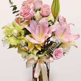 Pink roses and lilies arranged in a glass vase with a ribbon