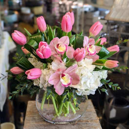 Pink tulips and orchids arranged in a clear glass vase with white hydrangeas.