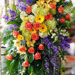 Large standing floral spray with orange roses, yellow orchids, and purple blooms