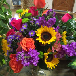 Mixed bouquet of roses, sunflowers, and purple flowers in a glass vase