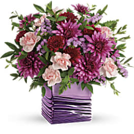 Purple and pink mixed flower arrangement in a square lavender vase