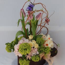 Pink tulips and mixed flowers in a dark box with decorative butterfly picks