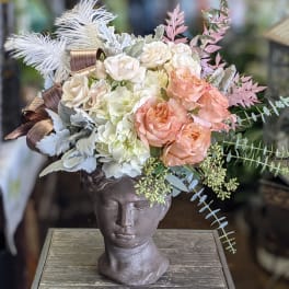 Floral arrangement in a sculpted head vase with cream and peach blooms