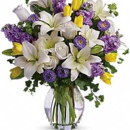 Bouquet of white lilies, purple flowers, and yellow tulips in a glass vase