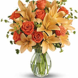Orange roses and pale lilies in a clear glass vase