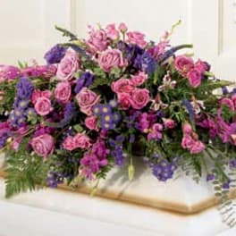 Large pink and purple floral casket spray on a white casket