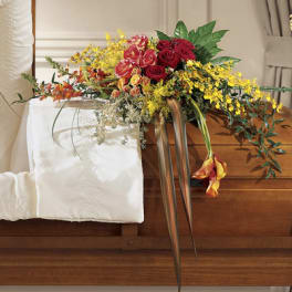 Casket spray with red roses, yellow flowers, and trailing greenery