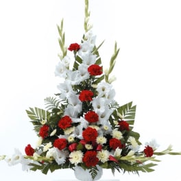 Tall red and white sympathy arrangement with carnations and mums in a white urn