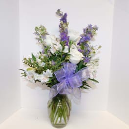 White and purple flower arrangement in a glass vase with a lavender bow