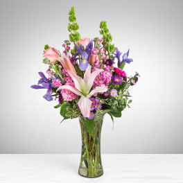 Tall mixed bouquet of pink lilies, roses, and purple blooms in a clear glass vase