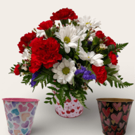 Red carnations and white daisies in a heart-print container with two empty heart-themed pots beside it