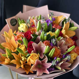 Mixed bouquet of lilies, roses, and purple flowers wrapped in pink paper