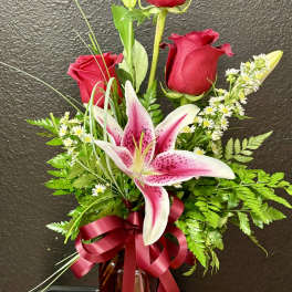 Tall arrangement of red roses and a pink stargazer-style lily in a red glass vase with ribbon