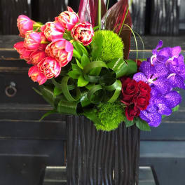 Colorful bouquet with tulips, roses, and purple orchids in a black vase