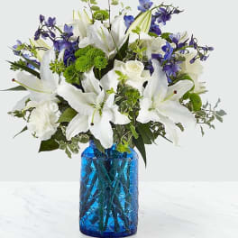 White lilies and blue flowers arranged in a blue glass vase