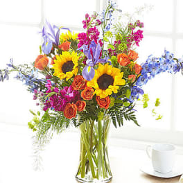 Colorful bouquet with sunflowers, roses, and blue flowers in a glass vase