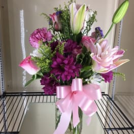 Pink and purple flower arrangement in a glass vase with a pink ribbon
