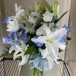 White lilies and blue flowers arranged in a clear glass vase.