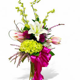Bouquet of lilies, hydrangea, and pink flowers in a glass vase with a magenta ribbon