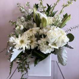 White floral arrangement in a square white vase with roses and lilies
