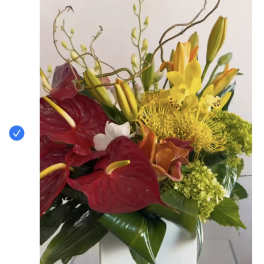 Tropical bouquet with red anthuriums, yellow lilies, and a white box vase