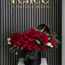 Red rose arrangement in a black hatbox with dark foliage