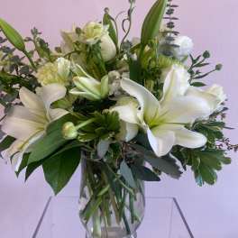 White lilies and mixed white flowers in a clear glass vase
