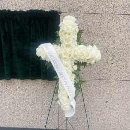 White rose funeral cross on a stand with a memorial ribbon