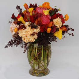Mixed bouquet of red, pink, and yellow flowers in a clear glass vase