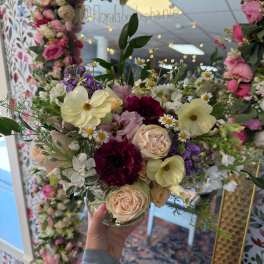 Mixed bouquet of pastel roses, daisies, and purple blooms in a glass vase